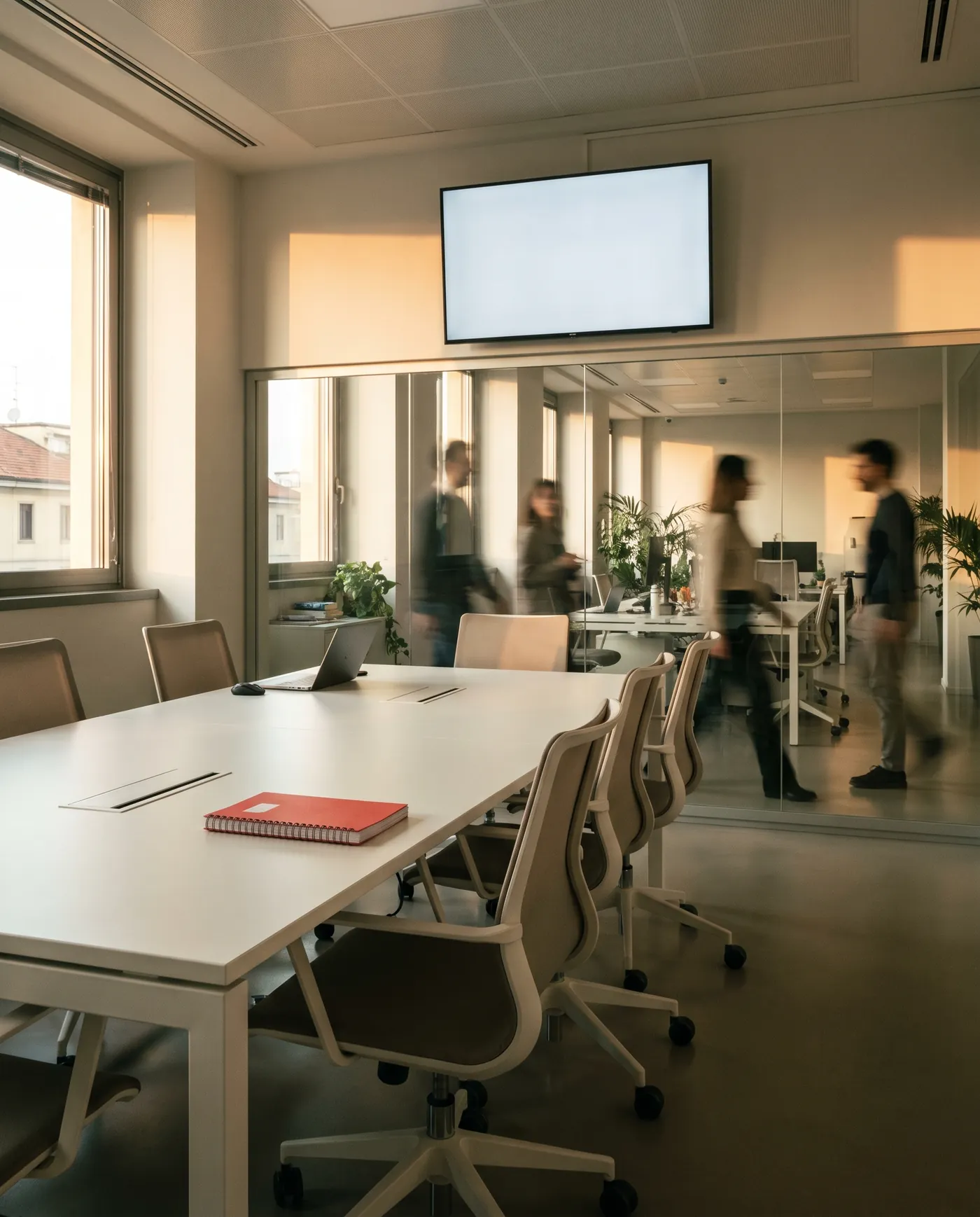Sala riunioni di un ufficio a Milano con colleghi in movimento dietro la vetrata